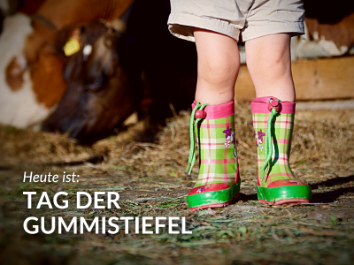 Bild von Kinderfüßen in Gummistiefeln mit Kuh im Hintergrund, dazu die Aufschrift: "Heute ist: Tag der Gummistiefel"